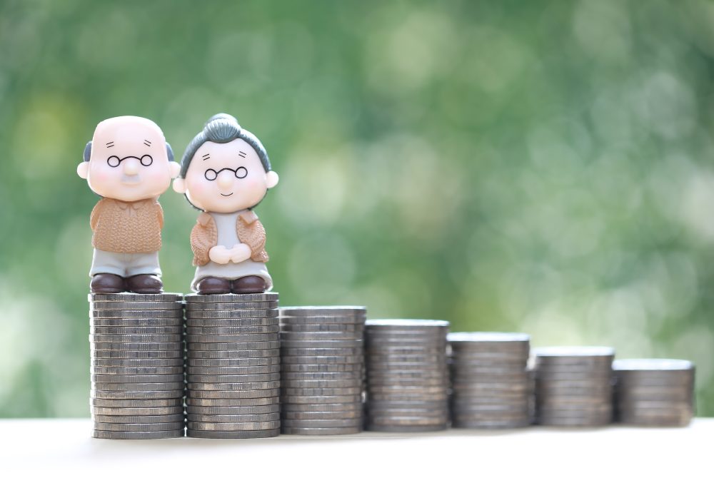 Senior couple and stack of coins on natural green background.